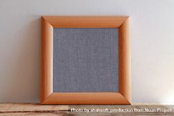 Plain square wooden picture frame with grey interior leaning against wall mockup bD9yA0