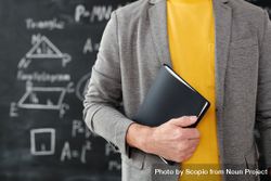 Cropped image of math teacher holding a book standing against chalkboard 0P2Bv4