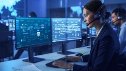 Network Specialist Monitors Complex System Diagrams on Dual Screens in Dimly Lit Control Room.