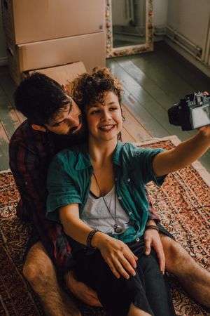 Joyful couple embracing and taking selfie on camera at home