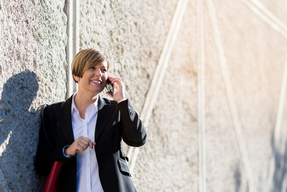 Happy female in blazer talking on smartphone outside on sunny day