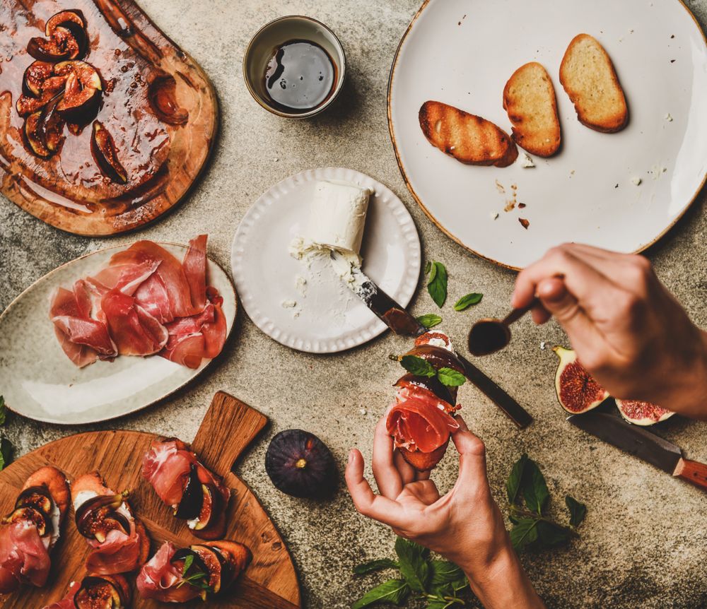 Crostinis with prosciutto, goat cheese and grilled figs, with hands holding spoon, square crop