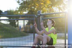 Teen sitting outdoors on basketball at a public court bG8lv0