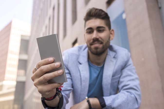 Happy man smiling while using his mobile phone standing outside