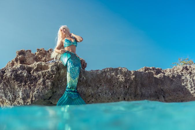 Blond fairytale female mermaid lying on rock