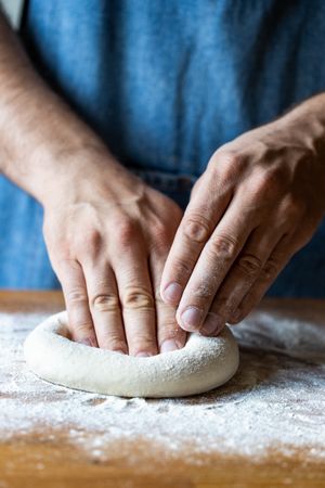Crop man flattening dough for pizza
