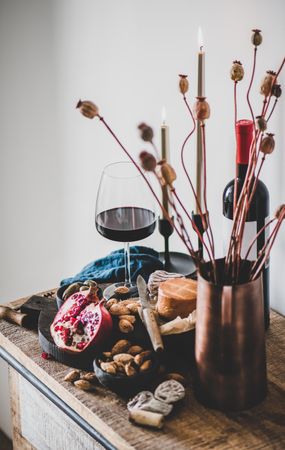 Rustic setting of wine, cheese, long candles, with pomegranate, and dried poppies, selective focus