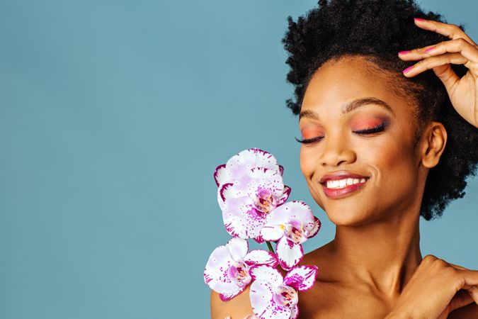 Studio beauty shot of a smiling Black woman with purple flowers and her eyes closed