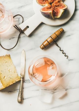 Rose wine in glass on marble table with quartered fig, cheese, and corkscrew