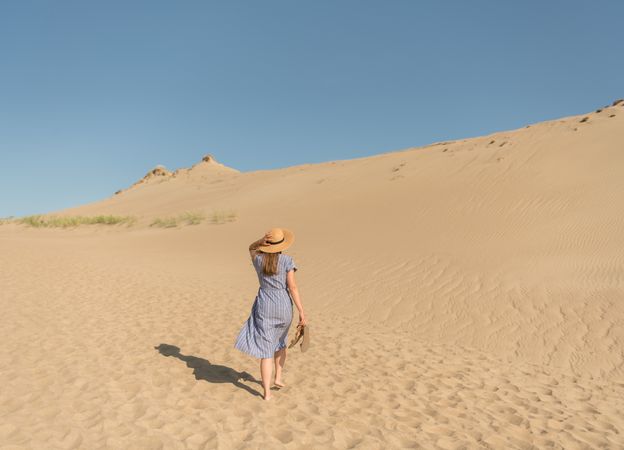 adult woman in casual dress and straw hat walking having good time on sand dune