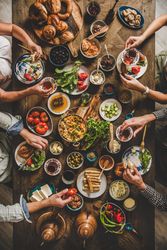 Group of people serving themselves at Turkish breakfast with eggs, breads, vegetables, and tea