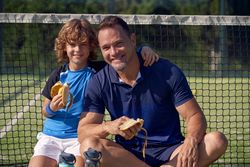 Smiling boy and trainer with bananas on court