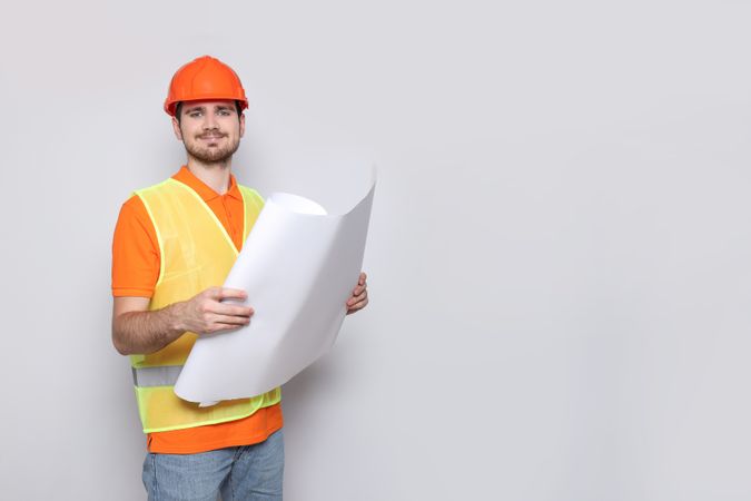Engineer in helmet with drawing paper in hands on gray background, space for text