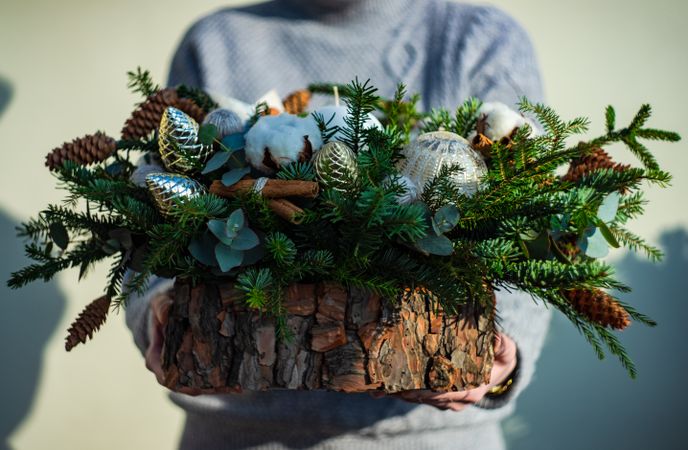 Person holding Christmas wooden centerpiece with branches and baubles