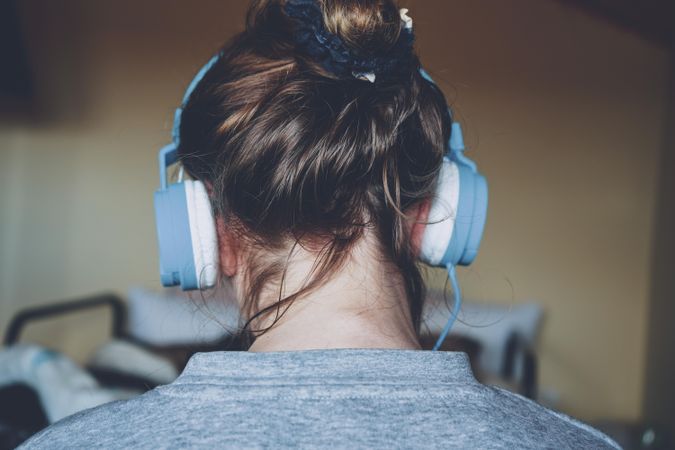 Back view of young woman in gray shirt wearing headphone