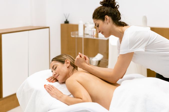 Masseuse putting elbow on female clients back