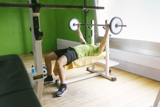 Man in green t-shirt lifting heavy bar exercising arms