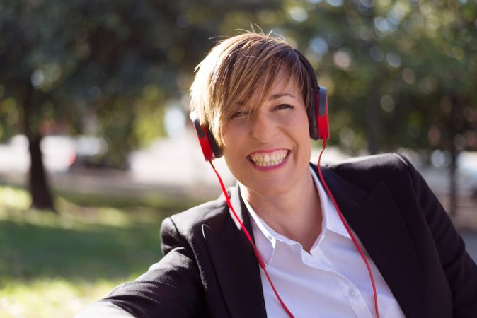Female in blazer sitting on park bench listening to music on red headphone
