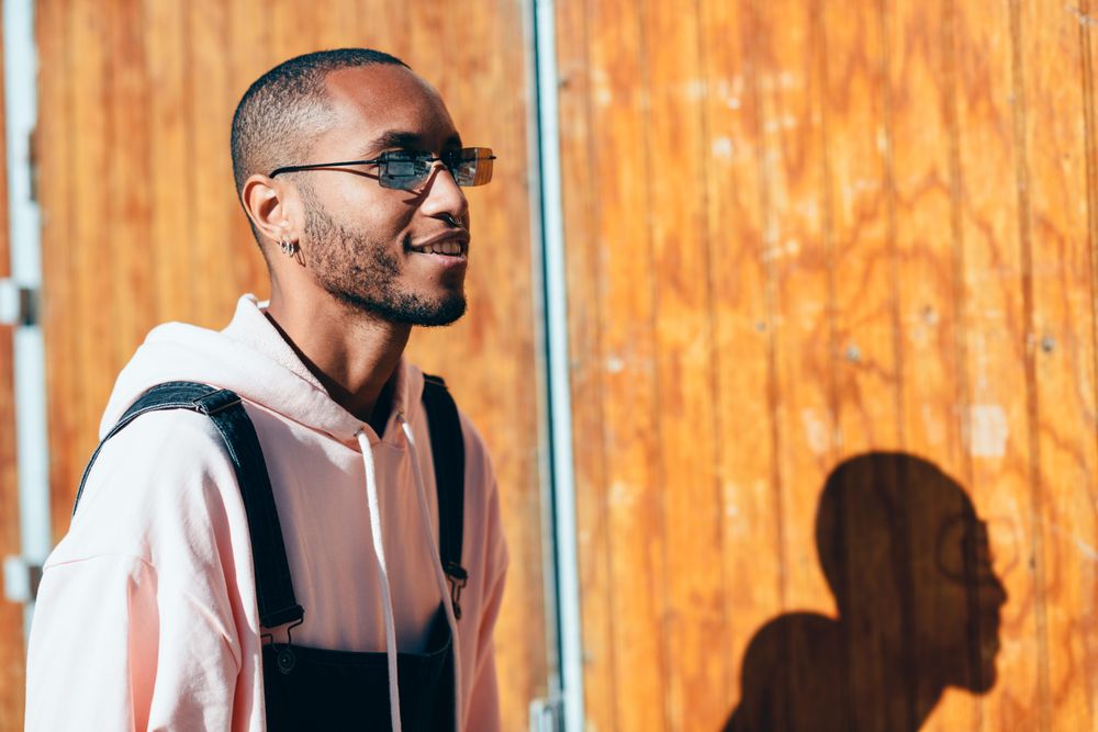 Male wearing overalls and happy and standing by a wooden wall