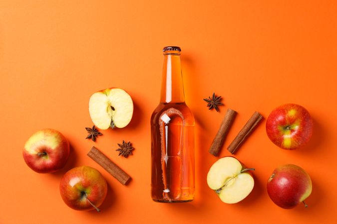 Composition with cider, apples and cinnamon on orange background