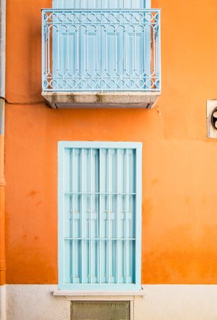Facade of bright orange wall with baby blue windows and balcony