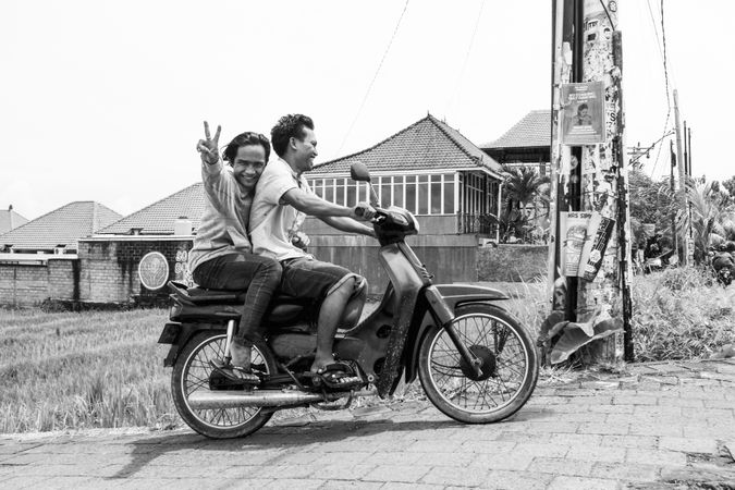 Bali, Indonesia - Feb 25, 2018 - Men riding moped, flashing peace sign