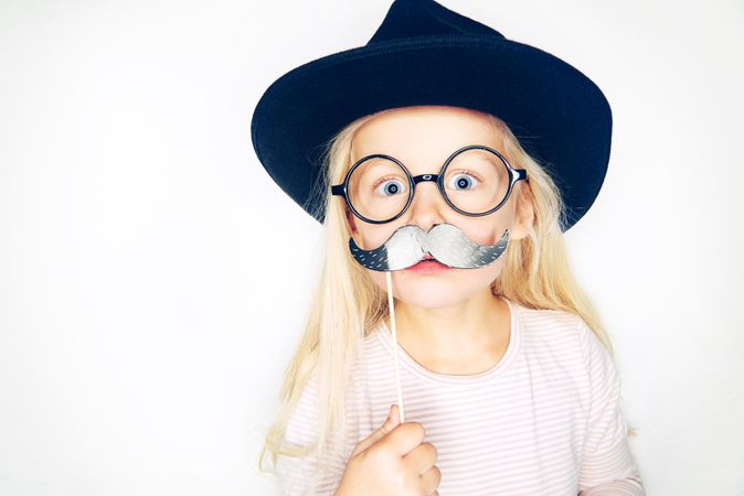 Blonde girl in hat and glasses with mustache on stick