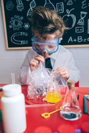 Kid doing soap bubbles with straw in glass