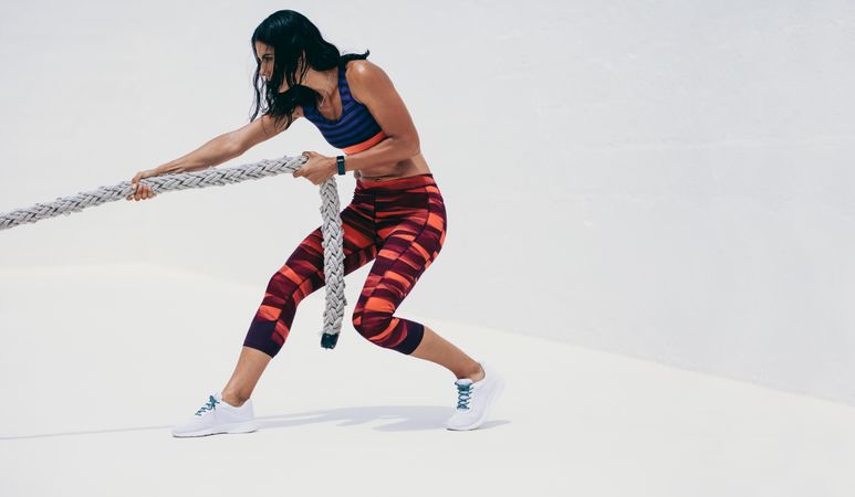 Fit young woman pulling battle rope during intense workout