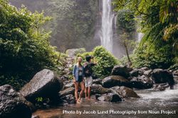 Friends standing in creek in front of tropical waterfall 4jZq34