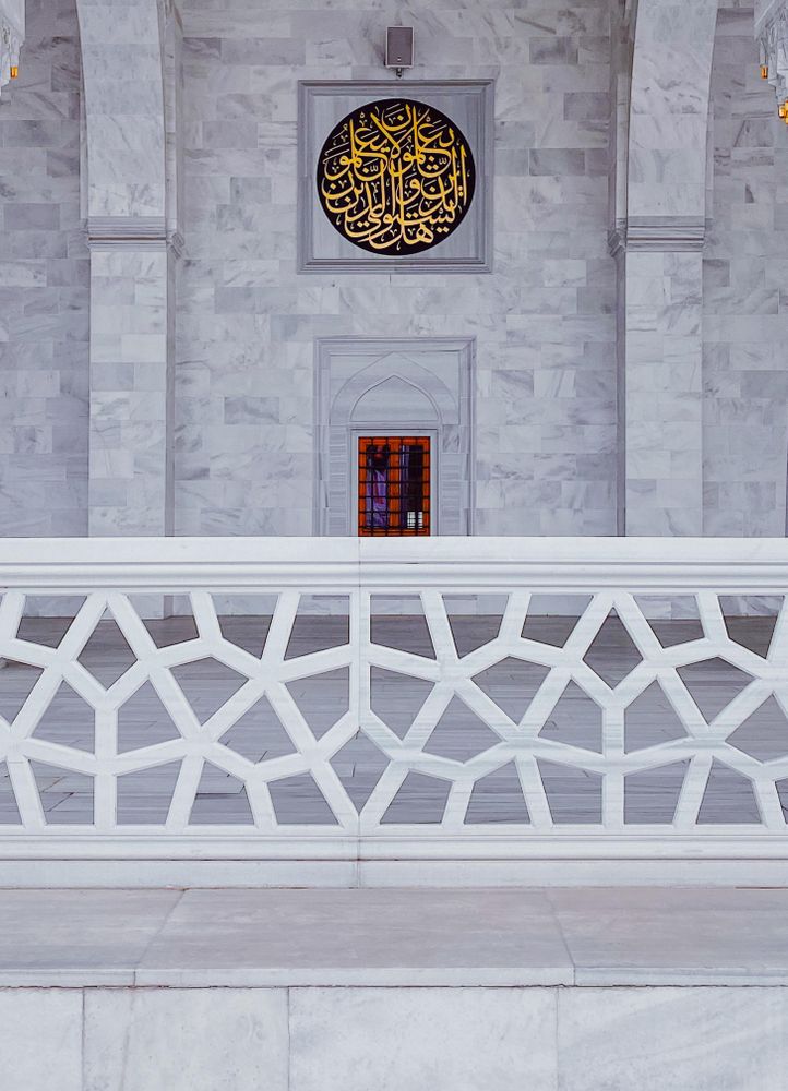 Marble wall in mosque with gold Arabic writing behind fence