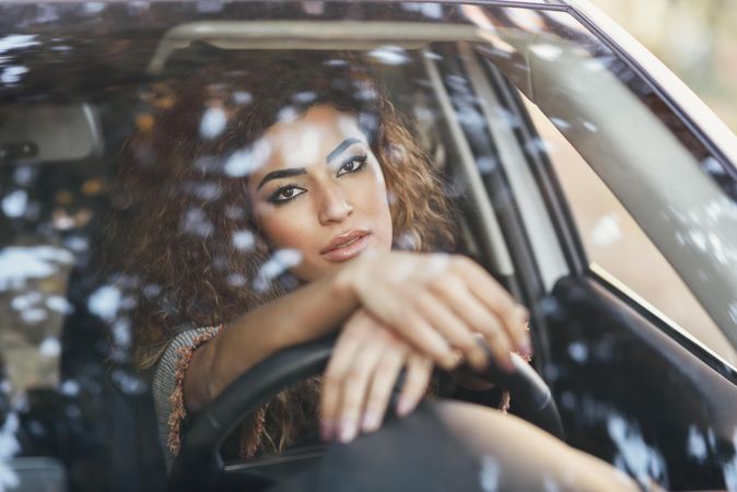Female with curly hair sitting in car with hands on steering wheel