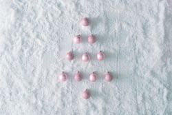 Wooden table background with snow and festive pink baubles in the shape of a tree