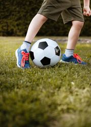 Cropped image of boy playing soccer ball on green grass field bYJw60