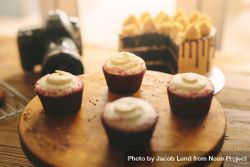 Close up shot of cupcakes on cake stand with camera and cake in background 47XkAb