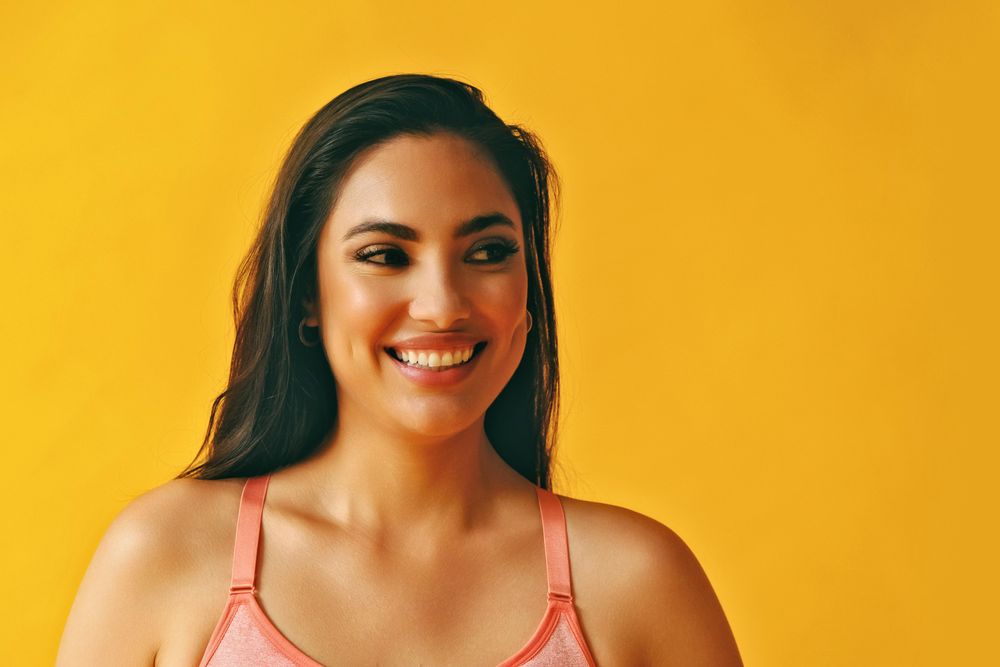 Headshot of smiling Hispanic woman looking to her side in a yellow room