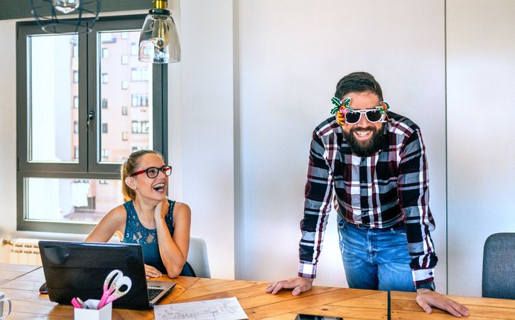 Businesswoman laughing looking at her colleague who is wearing funny glasses because he is going on vacation