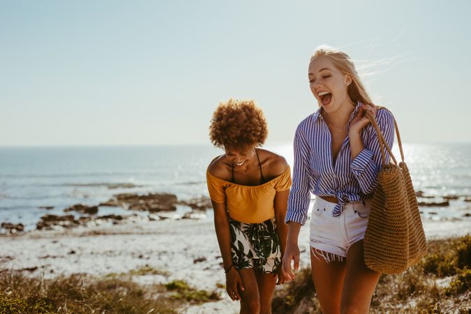 Female friends smiling while walking together at the seashore