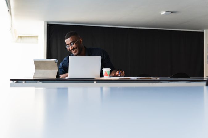 Black guy video chatting on tablet near laptop in workplace