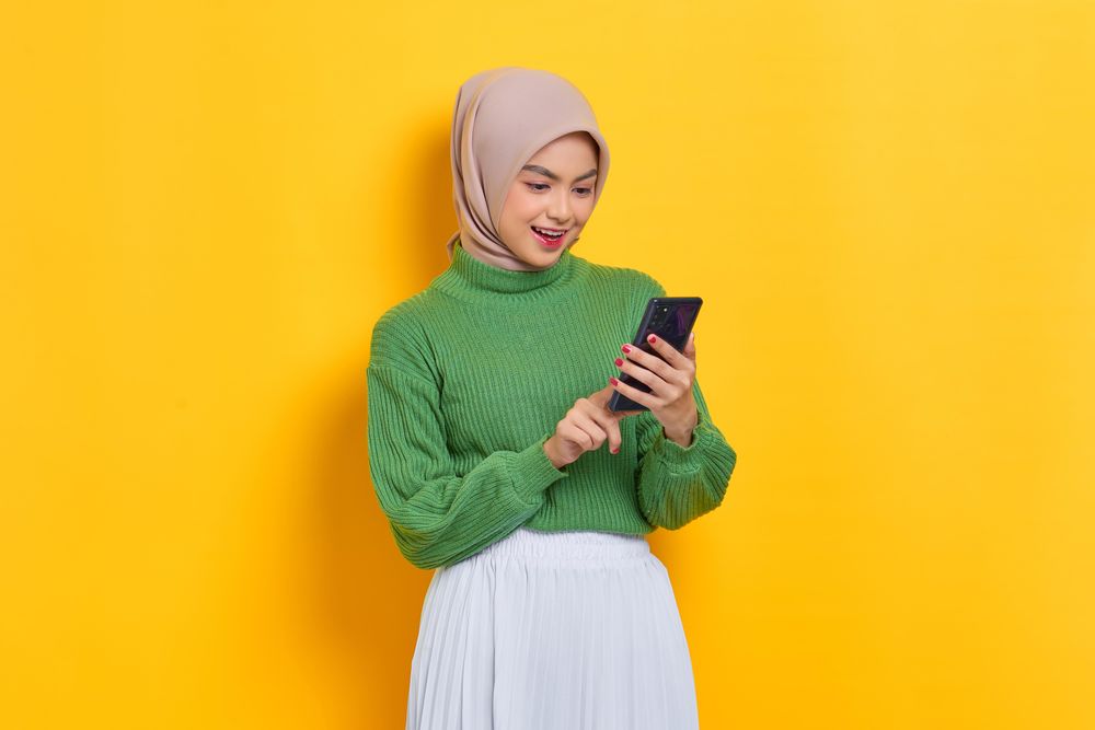 Calm woman in headscarf looking down and using her smart phone