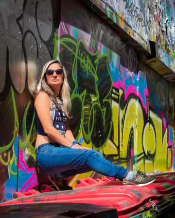Woman in crop top and blue denim jeans leaning on graffiti wall