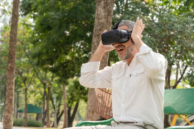 Mature grey haired man sitting outside in park wearing VR headset