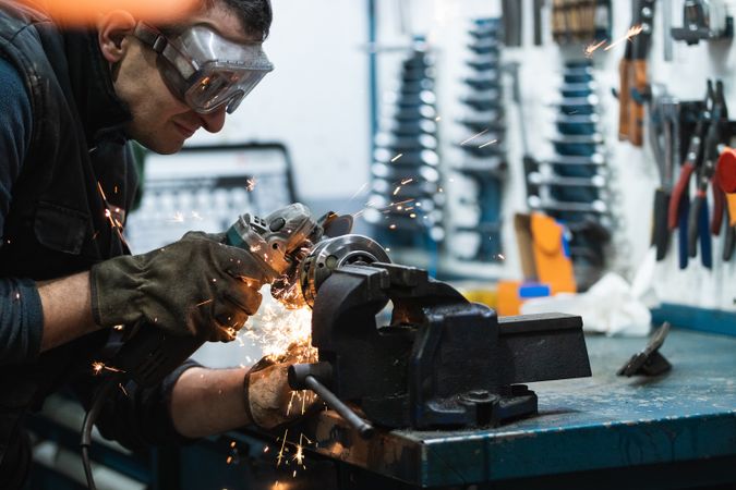 Attentive repairman cutting metal with electric grinder in workshop