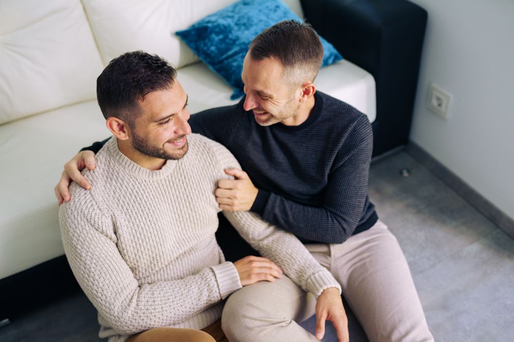 Cute male couple sitting on floor and talking at home