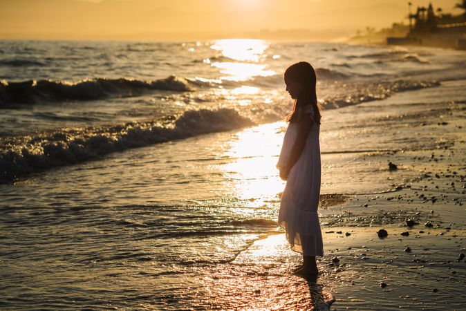 Adorable girl walking on seaside at sunset