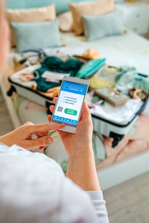 Woman preparing the suitcase and looking covid health passport on the mobile