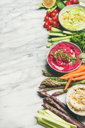 Fresh colorful vegetables and dips with hummus, avocados, asparagus, with copy space