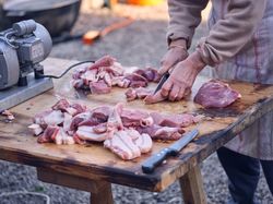 Crop person cutting raw meat with sharp knife on board