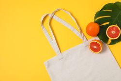 Eco bag, palm leaf and orange on color background, copy space