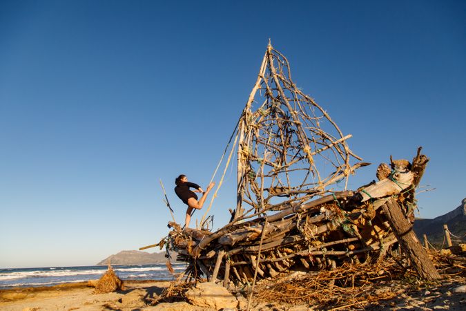 Young woman with upped leg on decorative wooden ship near water on shore